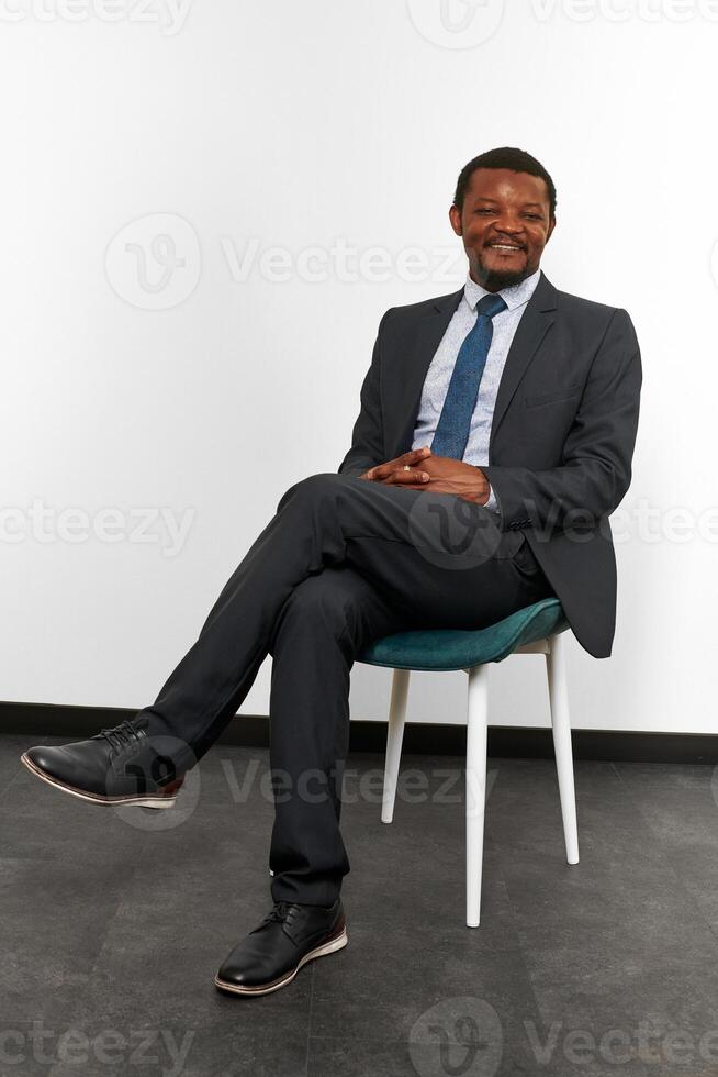 hombre negro afroamericano sonriente con traje de negocios sentado en una silla con los dedos cruzados foto