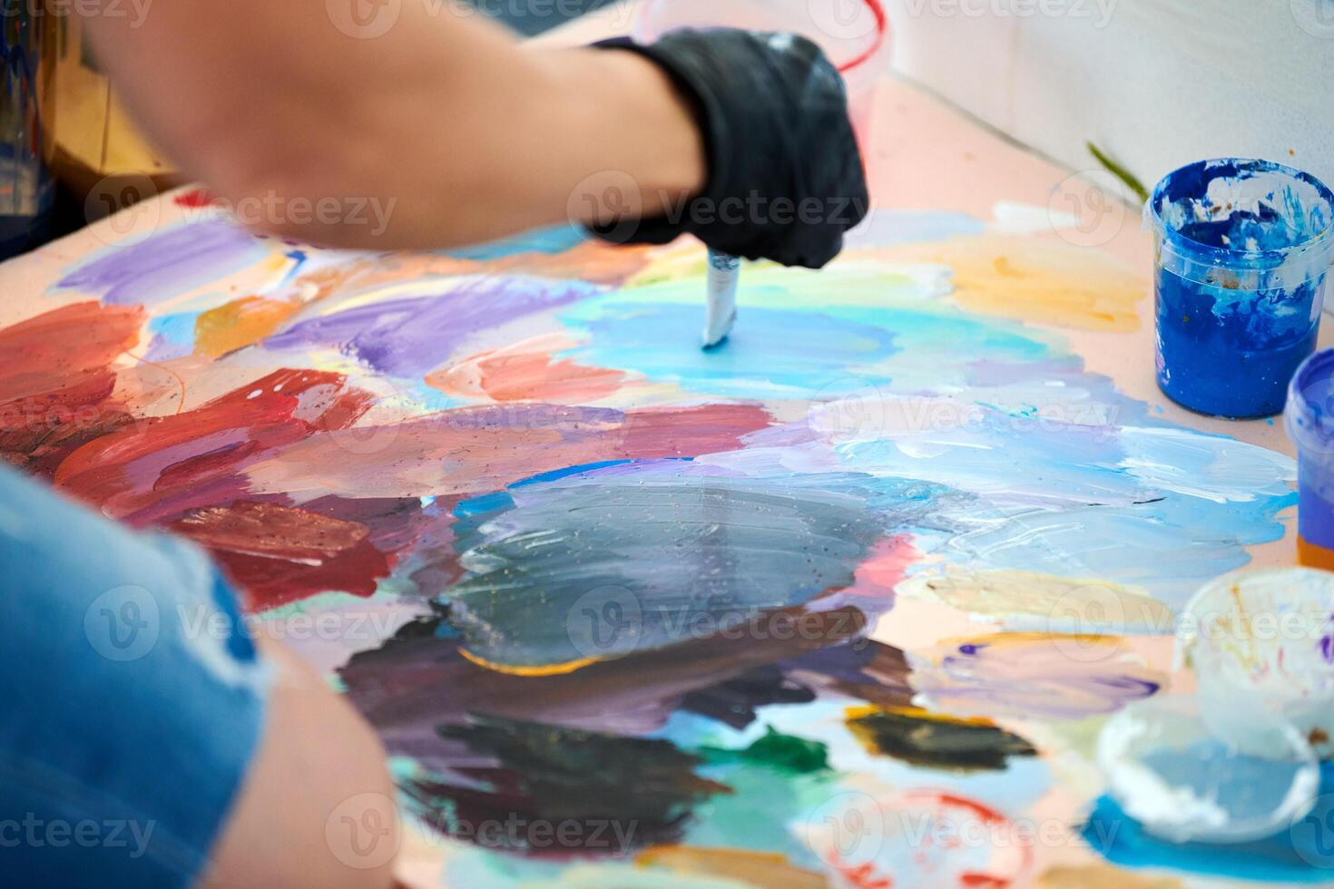 Artist hand in black gloves holds paint brush and choose color from colorful palette at art festival photo