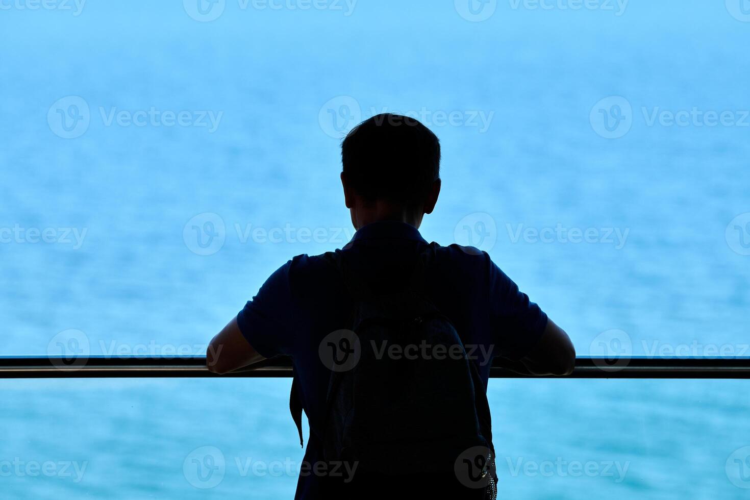 Silhouette of young man leaned on transparent glass handrail on above blue sparkling sea background photo