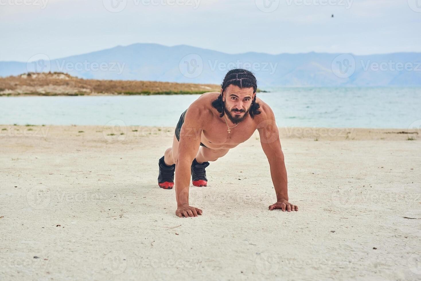 young muscular man exercising on the beach, young muscular man doing bodibuilding exercises on the beach, athletic young man on the beach photo