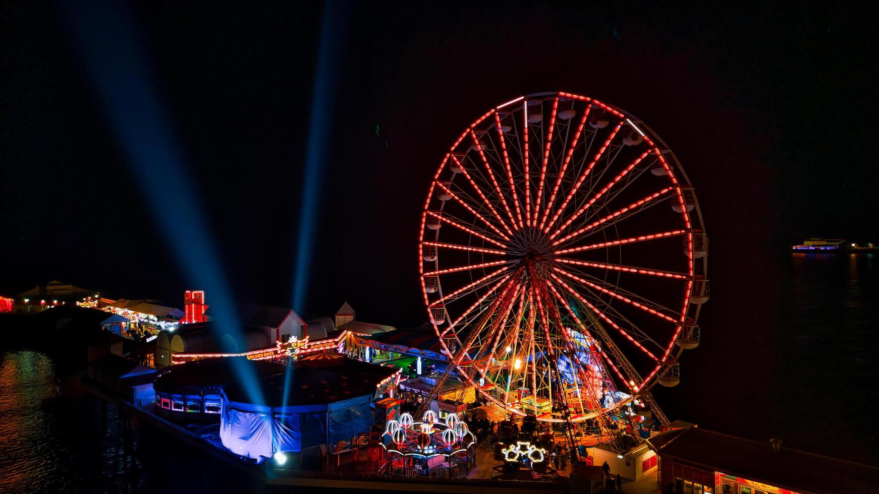 Illuminated ferris wheel at night with vibrant lights and beams against a dark sky. photo