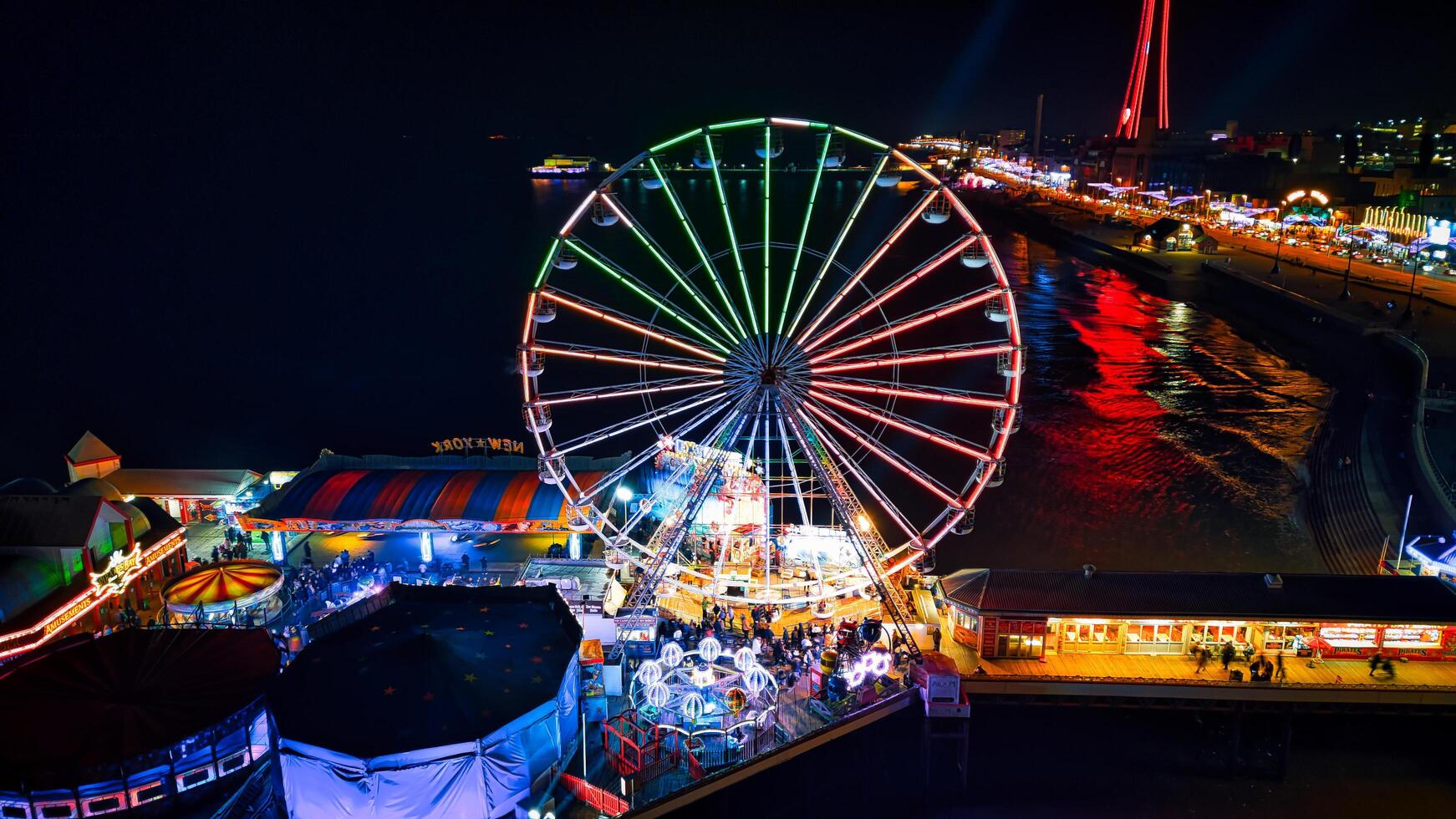 Colorful night view of a vibrant amusement park with a Ferris wheel and bright lights reflecting on water in Backpool, England. photo