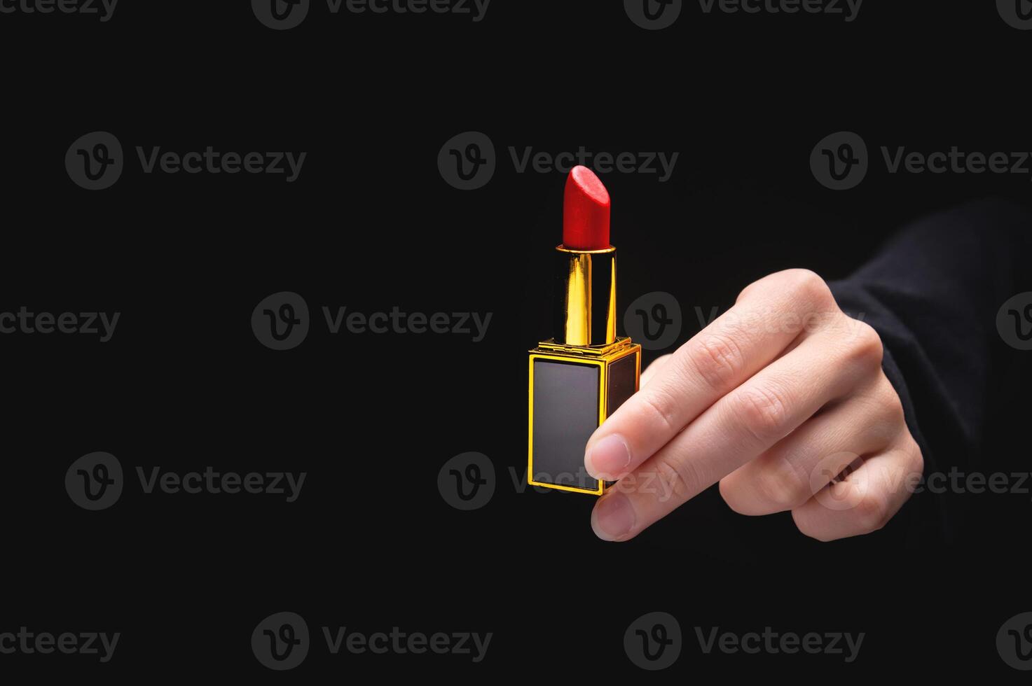 Red lipstick in a woman's hand on a dark background. Girl holding a popular cosmetic product photo