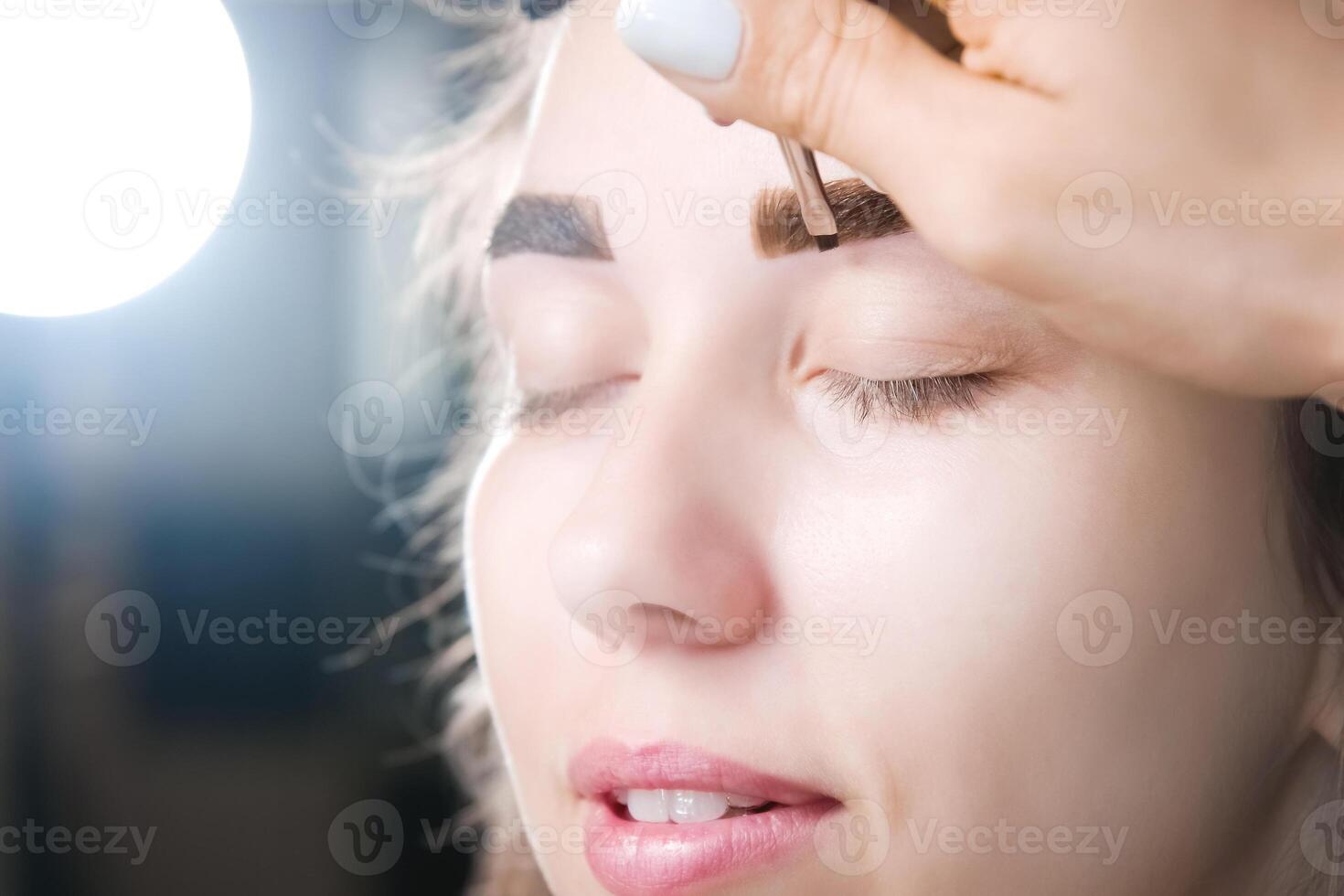 Eyebrow tinting. Close-up of a master applying eyebrow dye with a brush. Cosmetic procedures, permanent eyebrow makeup. correction and modeling of eyebrows in a beauty salon photo