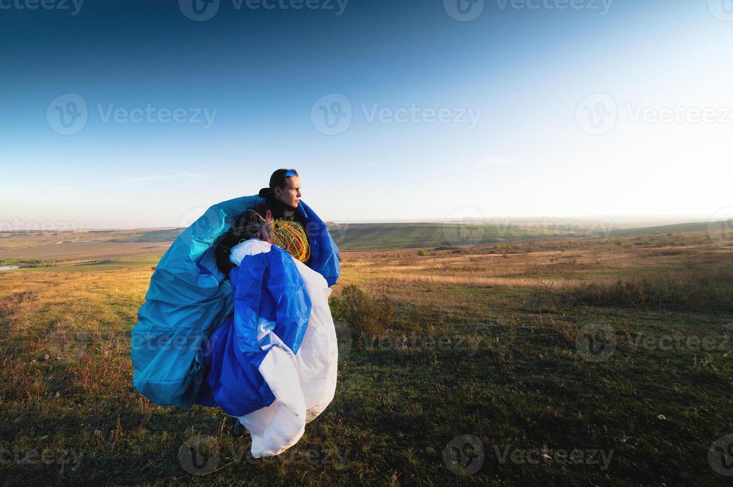 chico sostiene el líneas de un parapente en su manos de cerca. un masculino parapente lleva un parapente a un pastar. el piloto cheques el parapente líneas a garantizar ellos son no dañado. foto