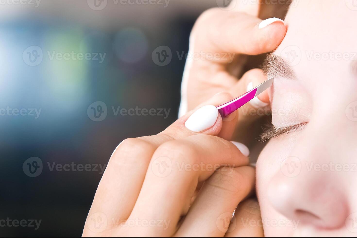 Extreme close-up of a young woman plucking eyebrow hair with tweezers in a beauty salon photo