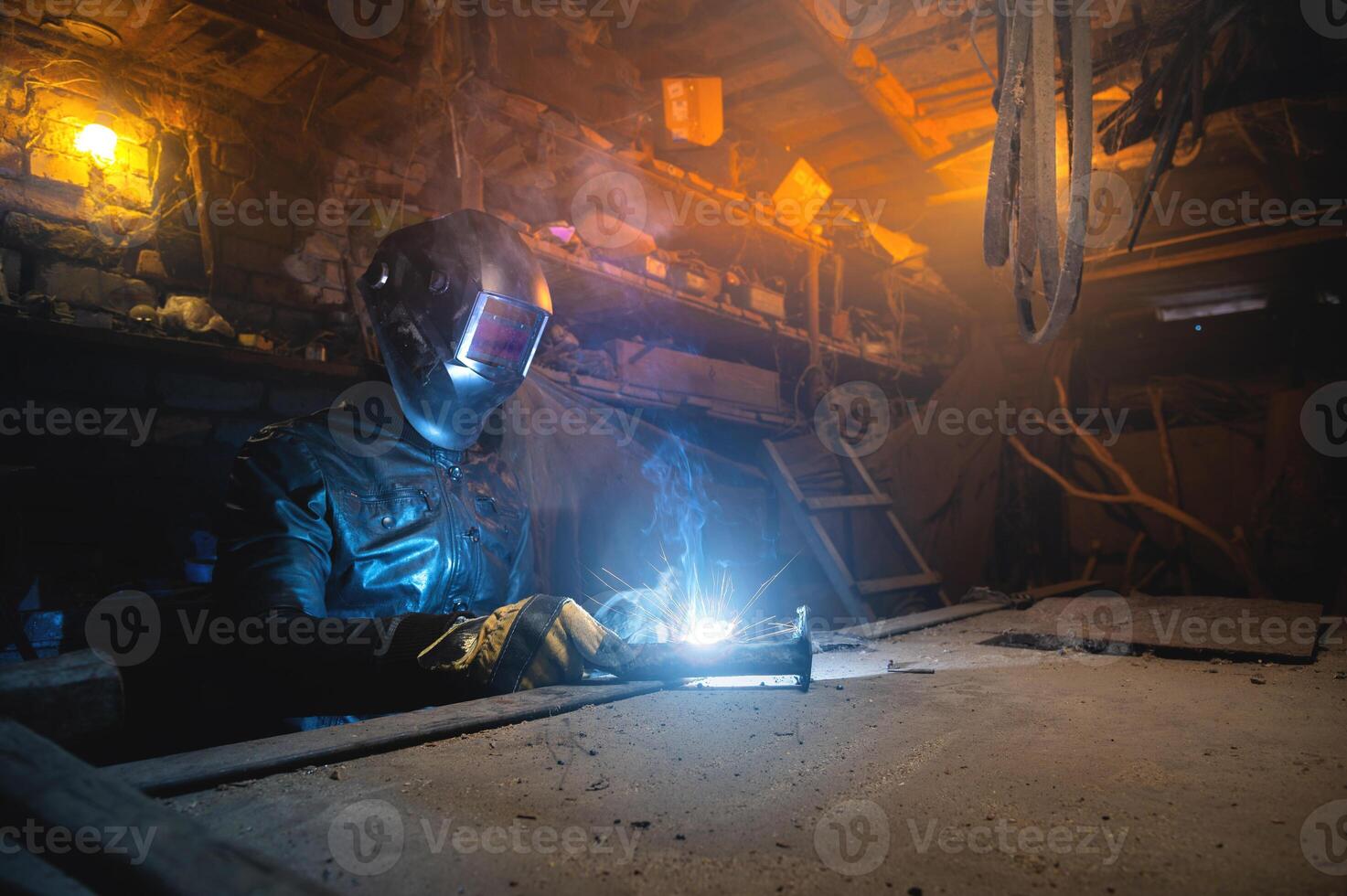 soldador en un taller soldaduras un metal parte. general plan de un antiguo desordenado garaje dónde un hombre en protector guantes y un máscara es haciendo foto