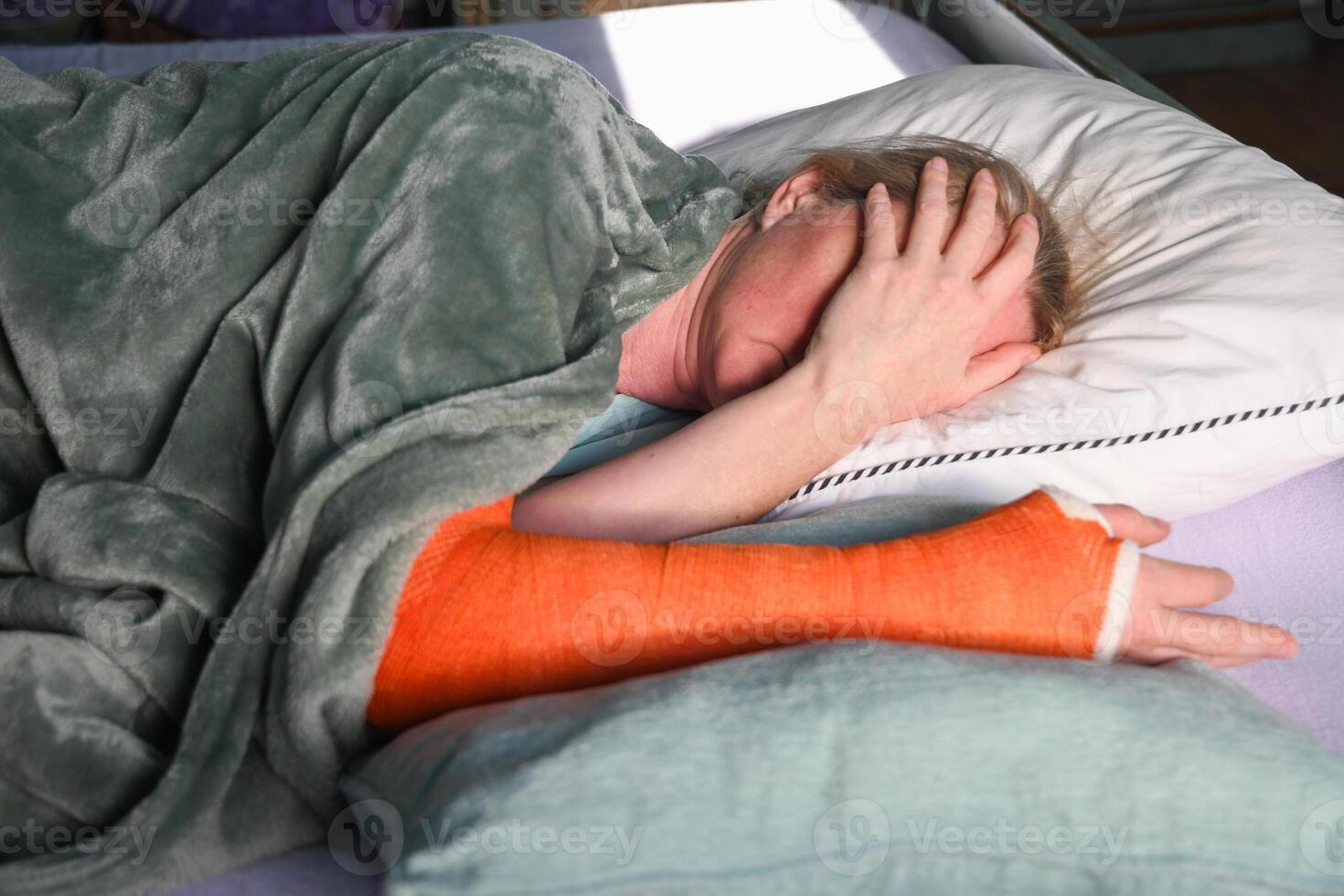woman with a broken right arm with an orange fiberglass plaster cast sleeps in bed with a pillow under the cast photo