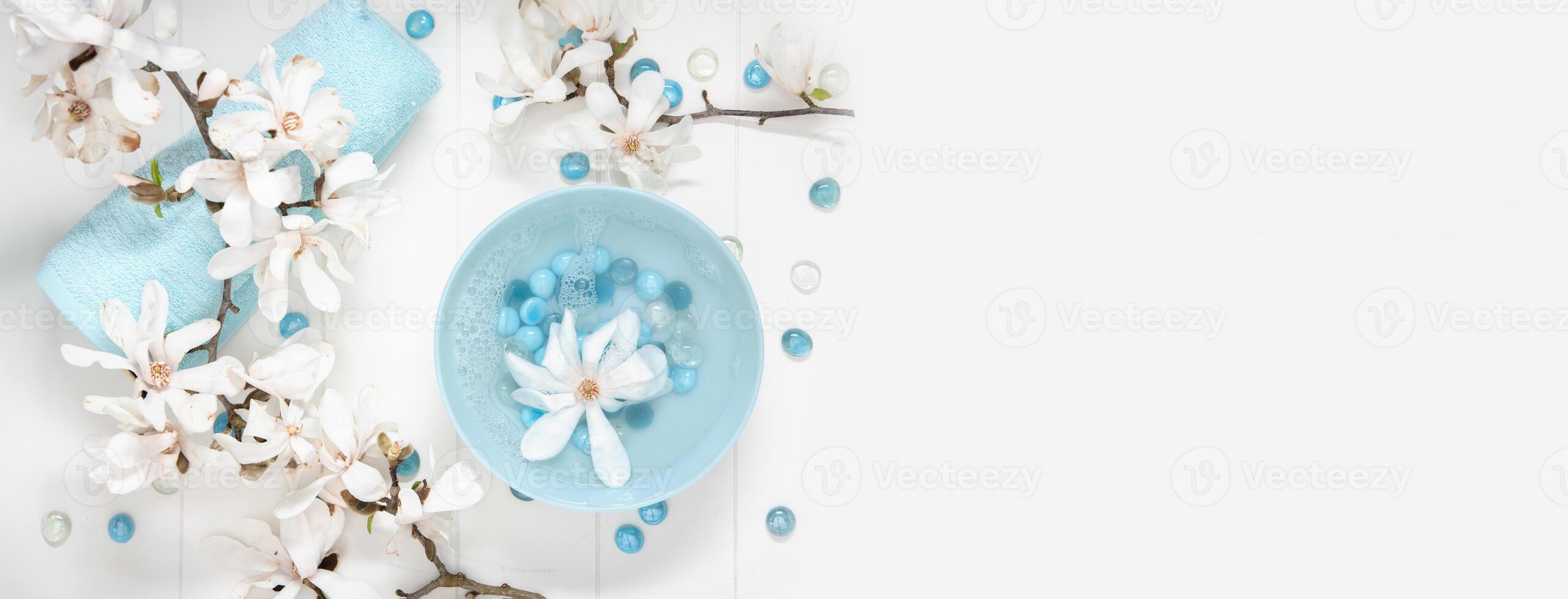 turquoise bowl with water and mother of pearl spa stones for gentle manicure in the salon with white magnolia flowers photo