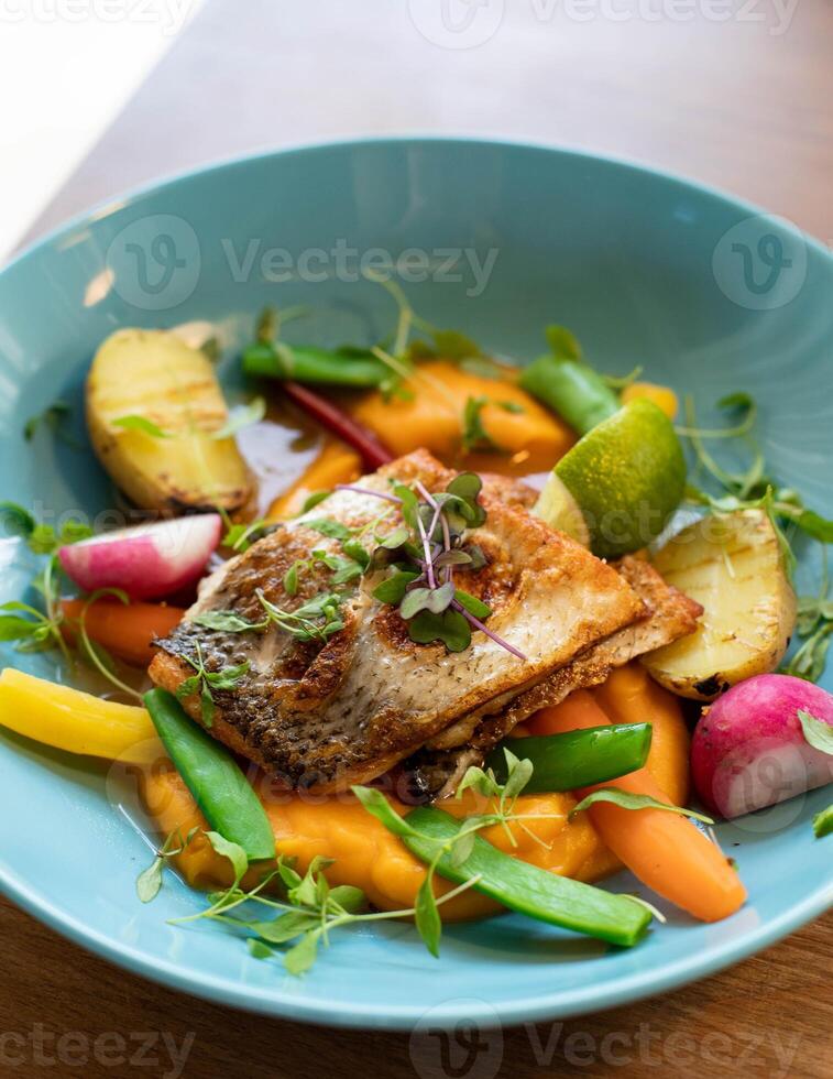 Fried fish with vegetables in a blue plate on a wooden table photo