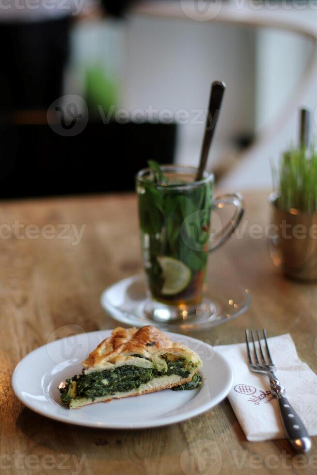 Slice of spinach pie on a white plate with a cup of tea photo