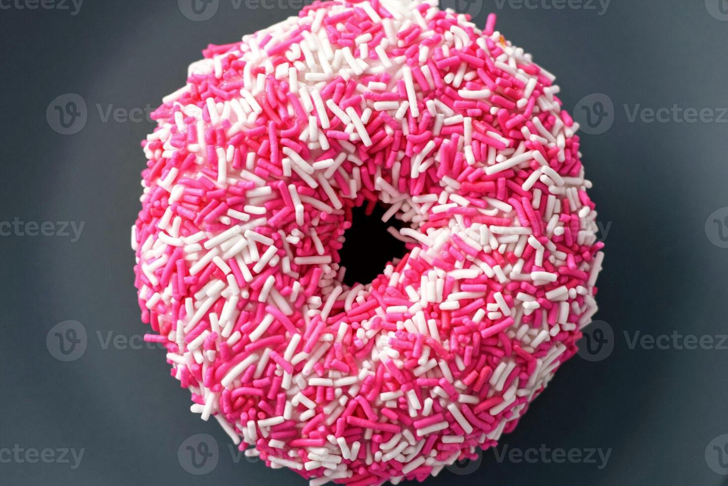 Pink donut with sprinkles on a dark background, top view photo