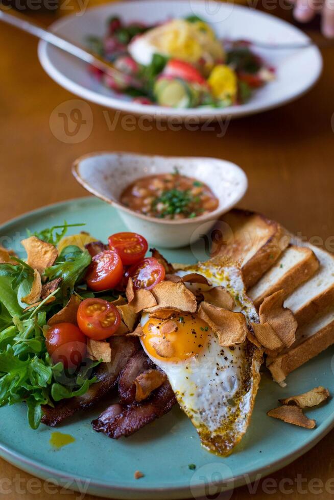 Breakfast with fried eggs, bacon, toasts and vegetable salad photo