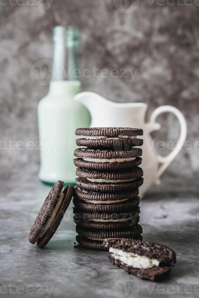 chocolate galletas con crema relleno y un botella de Leche en un gris antecedentes foto