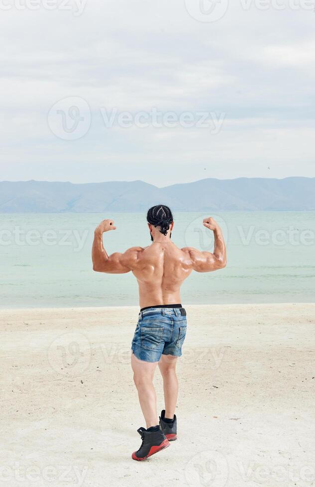 young muscular man exercising on the beach, young muscular man doing bodibuilding exercises on the beach, athletic young man on the beach photo