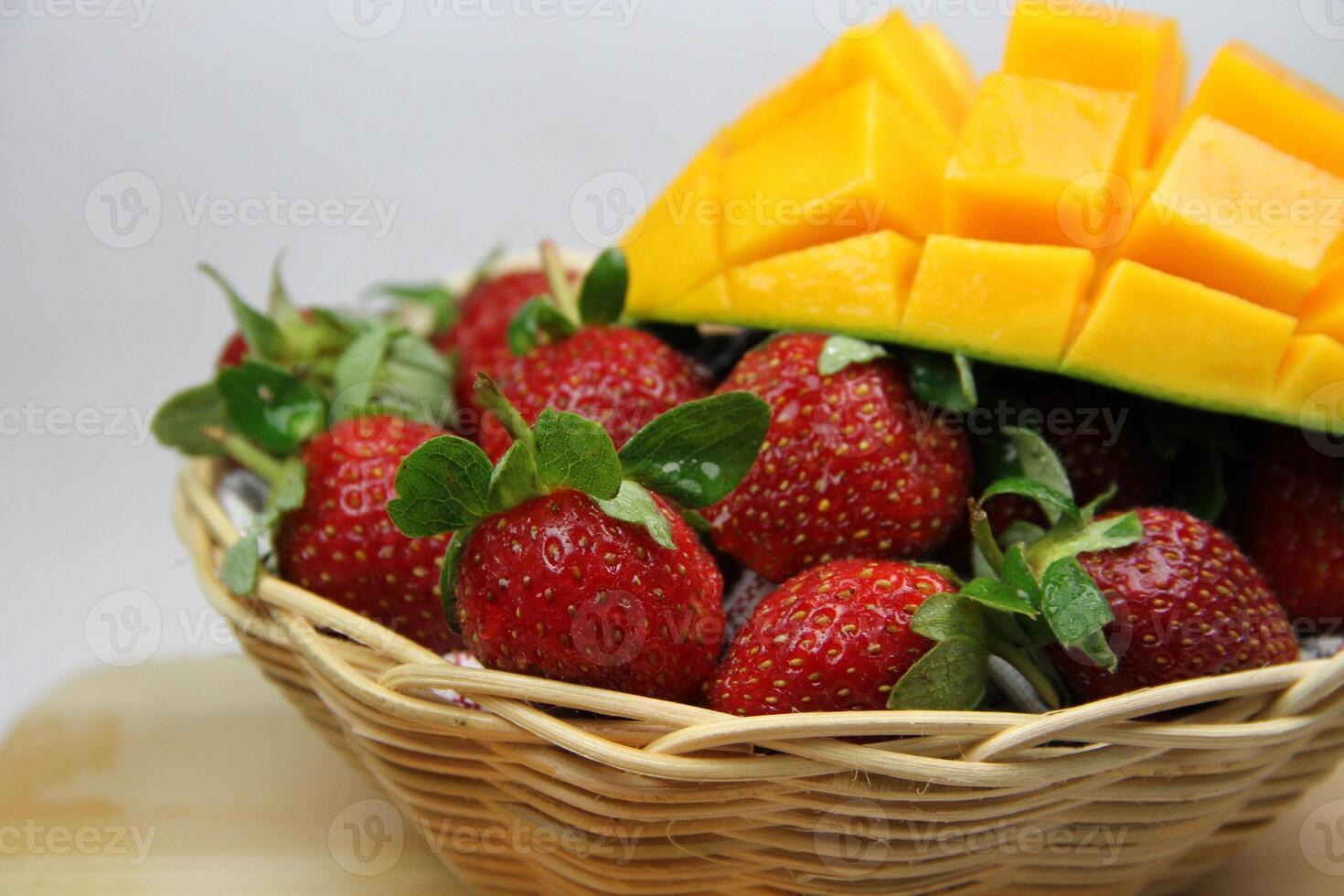 a basket of strawberries and mangoes on the cutting board on white background photo