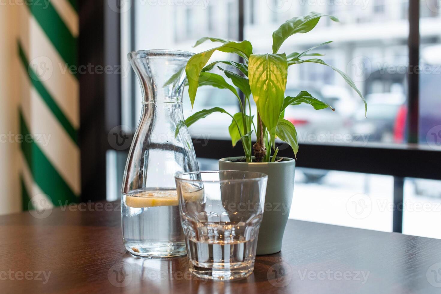 A decanter of water and lemon stands on the table next to a flower and a glass. healthy drink photo