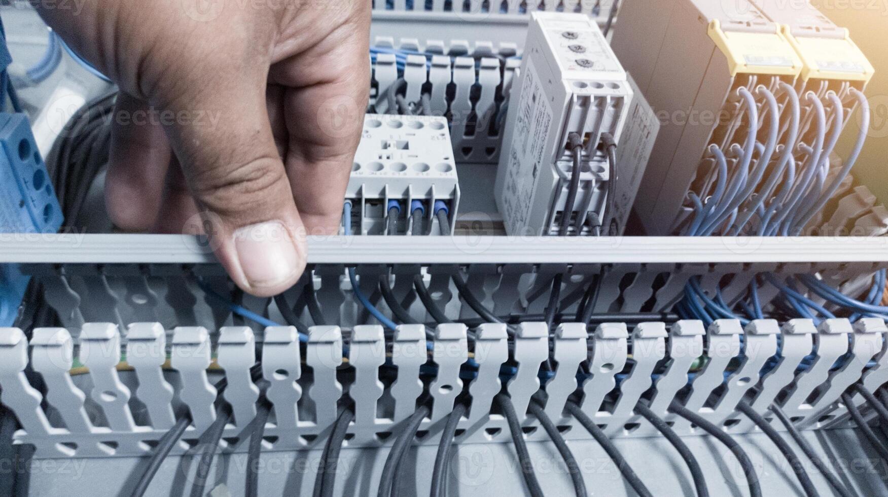 an electrician's hand is opening or closing the circuit cable cover on the electrical control panel board.Check and repair electrical trouble concept. photo