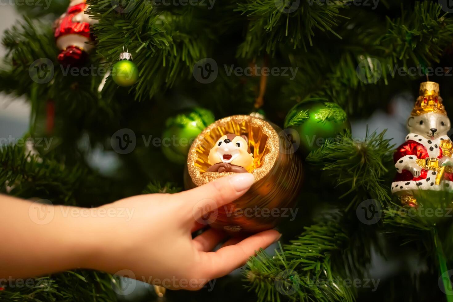 Hands decorating christmas tree with stylish bauble in atmospheric festive room. Merry Christmas. Winter holidays preparation photo