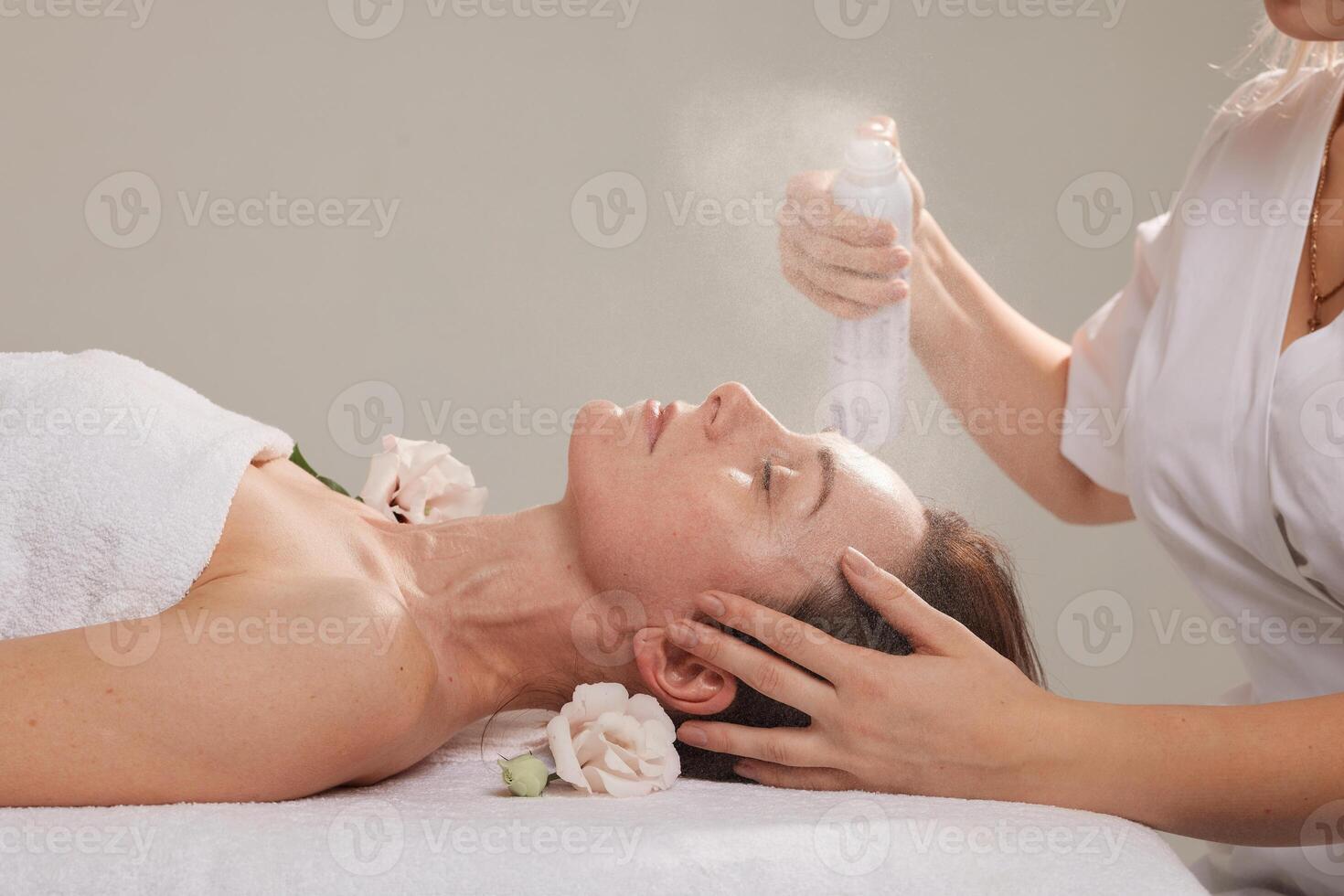 cosmetóloga aerosoles un refrescante rociar en un niña cara en un blanco antecedentes foto