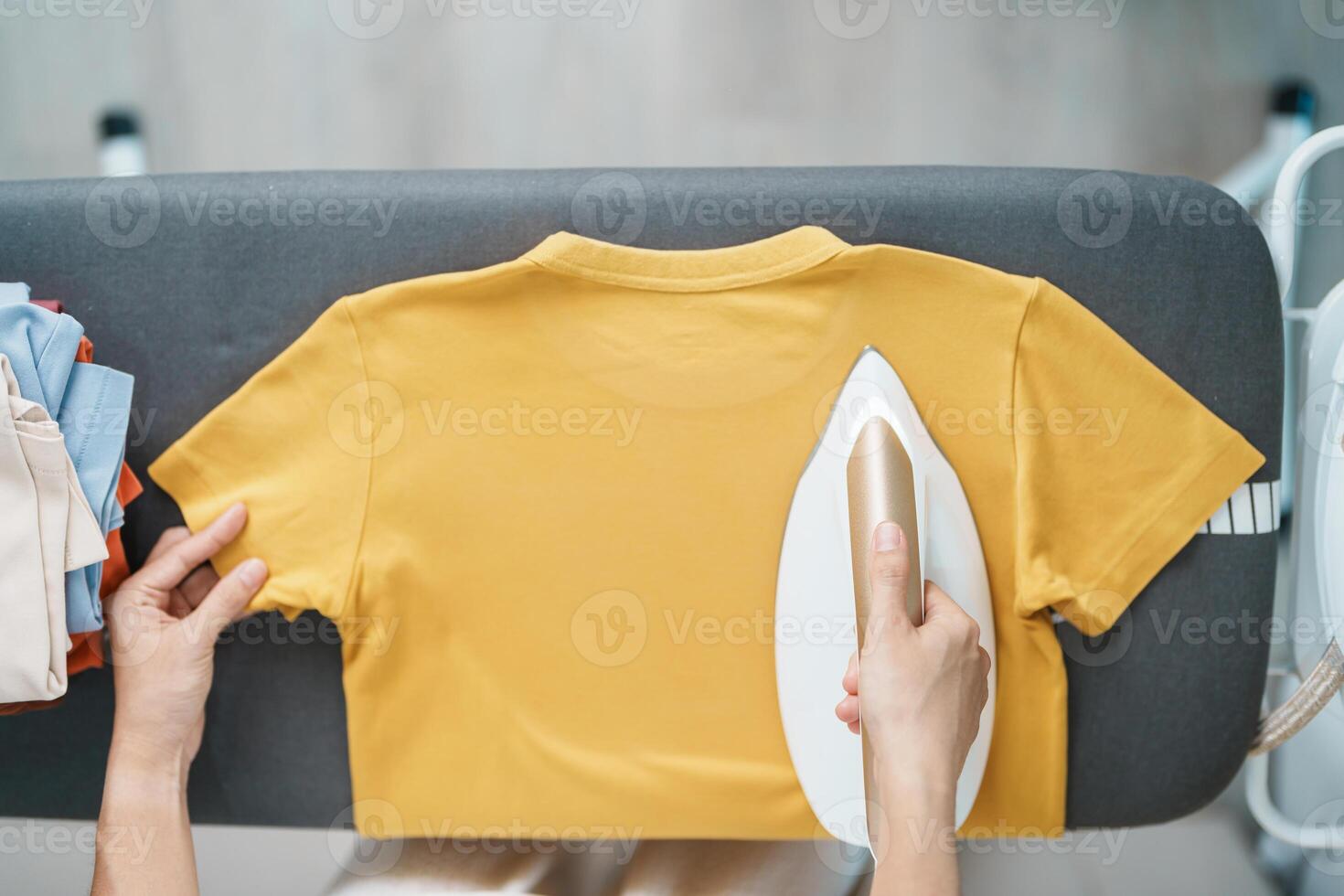 Woman hold Electric hot iron press T shirt clothes on ironing board, Intelligent automatic steam iron. Laundry, Housework, Housekeeping, Domestic hygiene, household of chores and daily routine concept photo