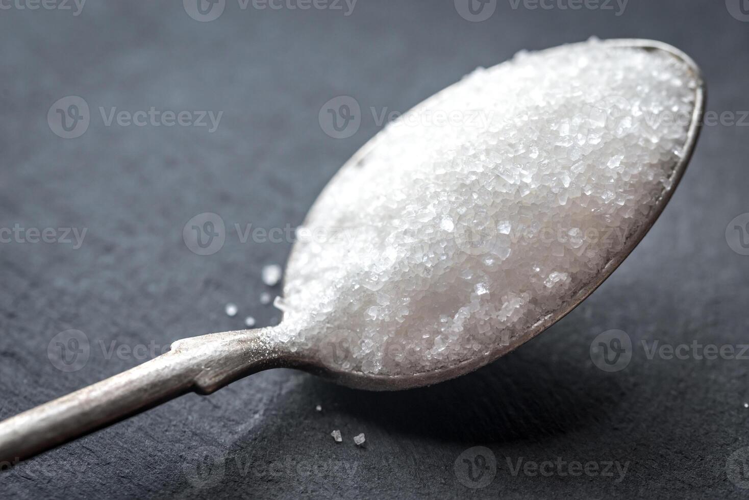 Spoon with white sugar on the dark background photo