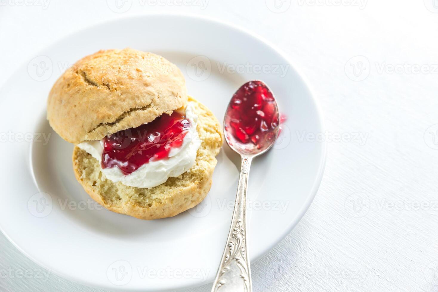 Scone with cream and cherry jam on the plate photo