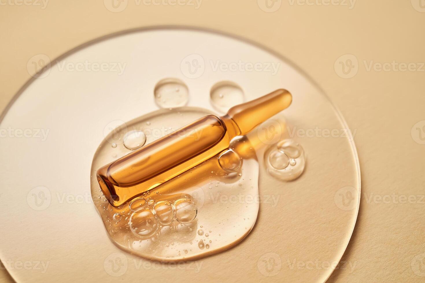 Ampoule in a drop of cosmetic gel on a beige background. photo