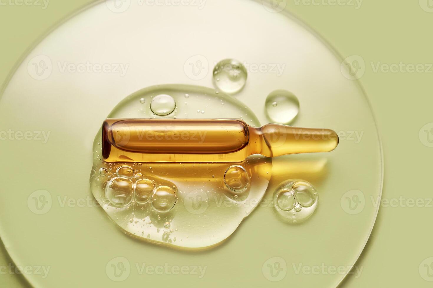 Ampoule in a drop of cosmetic gel on a green background. photo