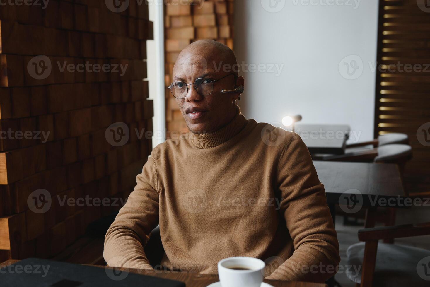 African-Ameican entrepreneur wearing shirt with rolled up sleeves looking through window with thoughtful and serious face expression, feeling nervous before meeting with business partners at cafe. photo