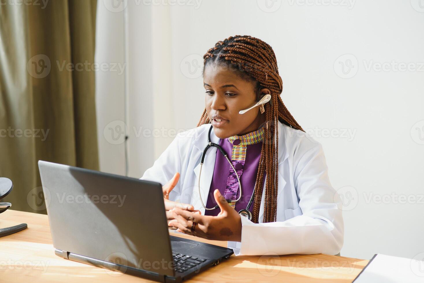 Smiling african american female doctor gp wears white medical coat using laptop computer at workplace gives remote online consultation, working on pc, consulting patient in internet telemedicine chat photo