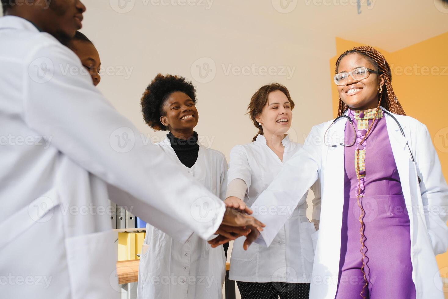 Mature doctors and young nurses stacking hands together at hospital. Close up hands of medical team stacking hands. Group of successful medical doctors and nurses stack of hands photo