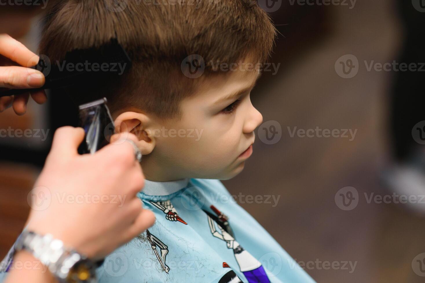 A little cute boy sits in a hairdresser's at the stylist's, a schoolchild is getting hair cut in a beauty salon, a child at a barbershop's, a short men's haircut photo