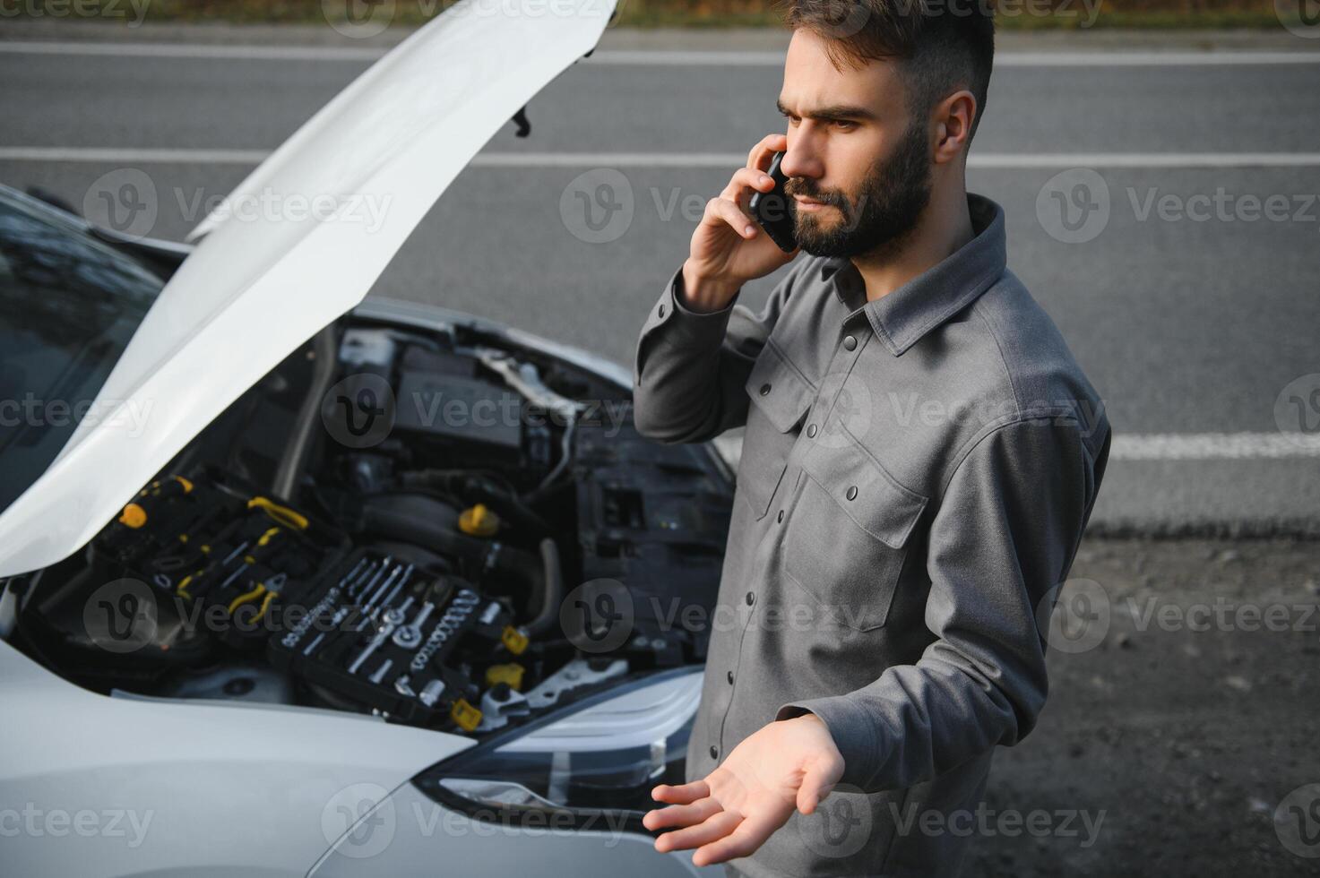 Sad driver calling car service, opening hood, having engine problem standing near broken car on the road. Car breakdown concept photo