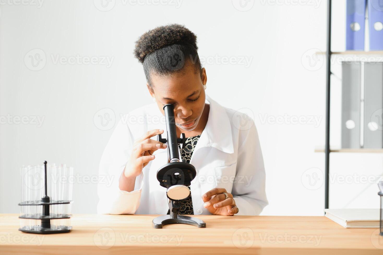 african american female lab technician looking through microscope in lab. photo