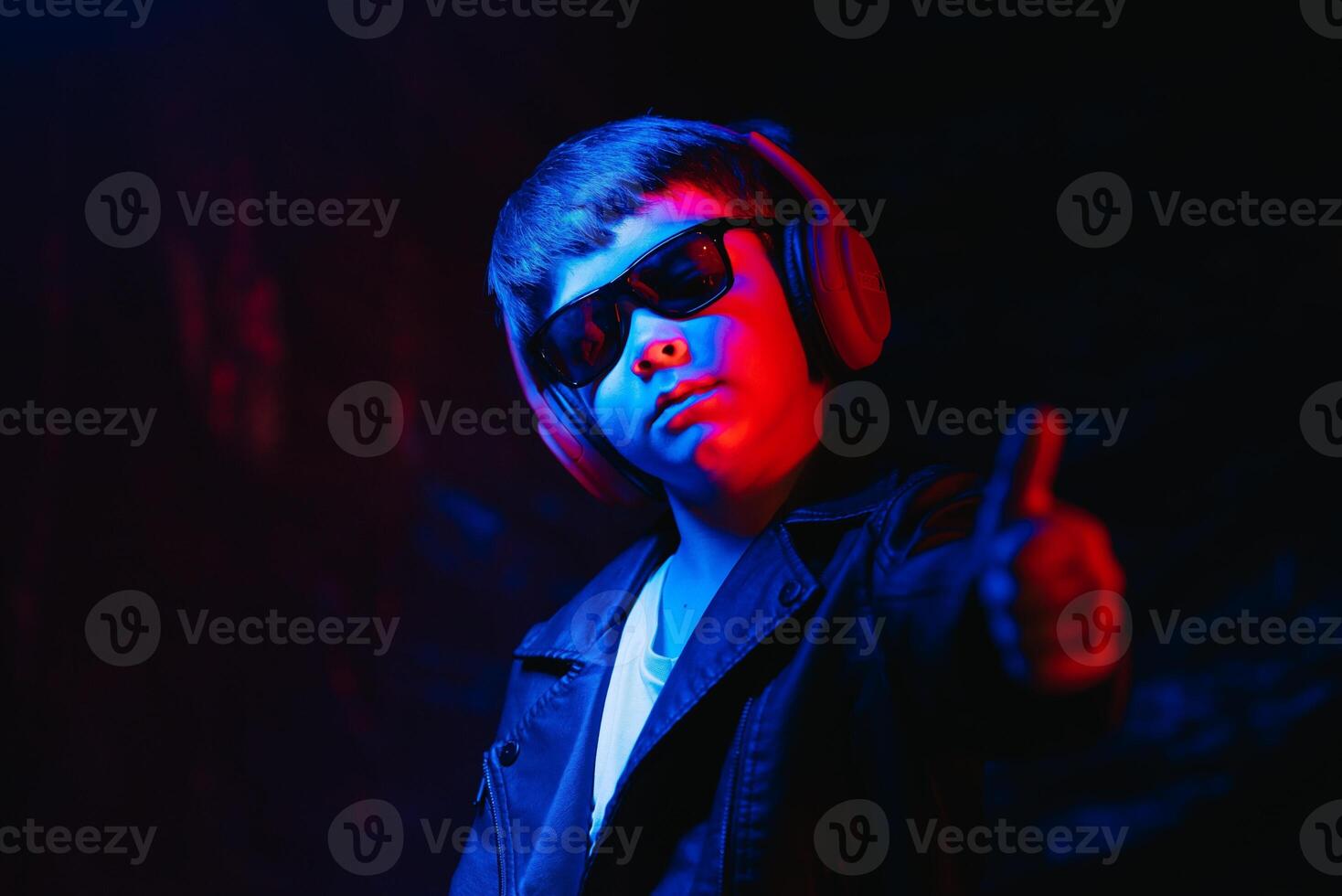 teen boy listening to music with headphones, neon light trending portrait. Looks at the camera photo