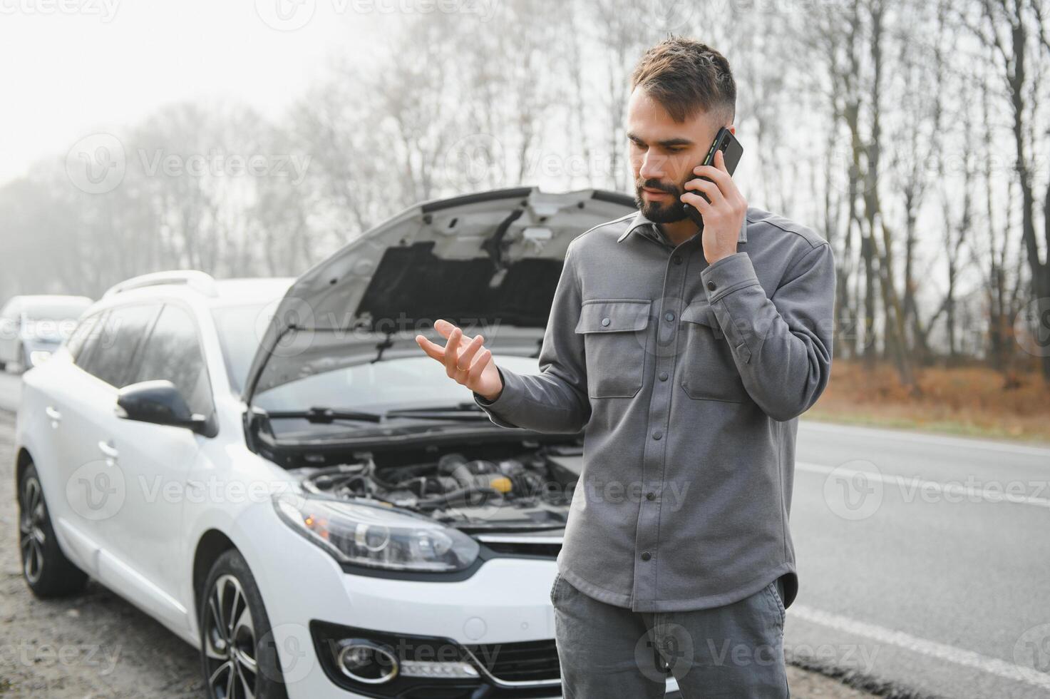 Sad driver calling car service, opening hood, having engine problem standing near broken car on the road. Car breakdown concept photo