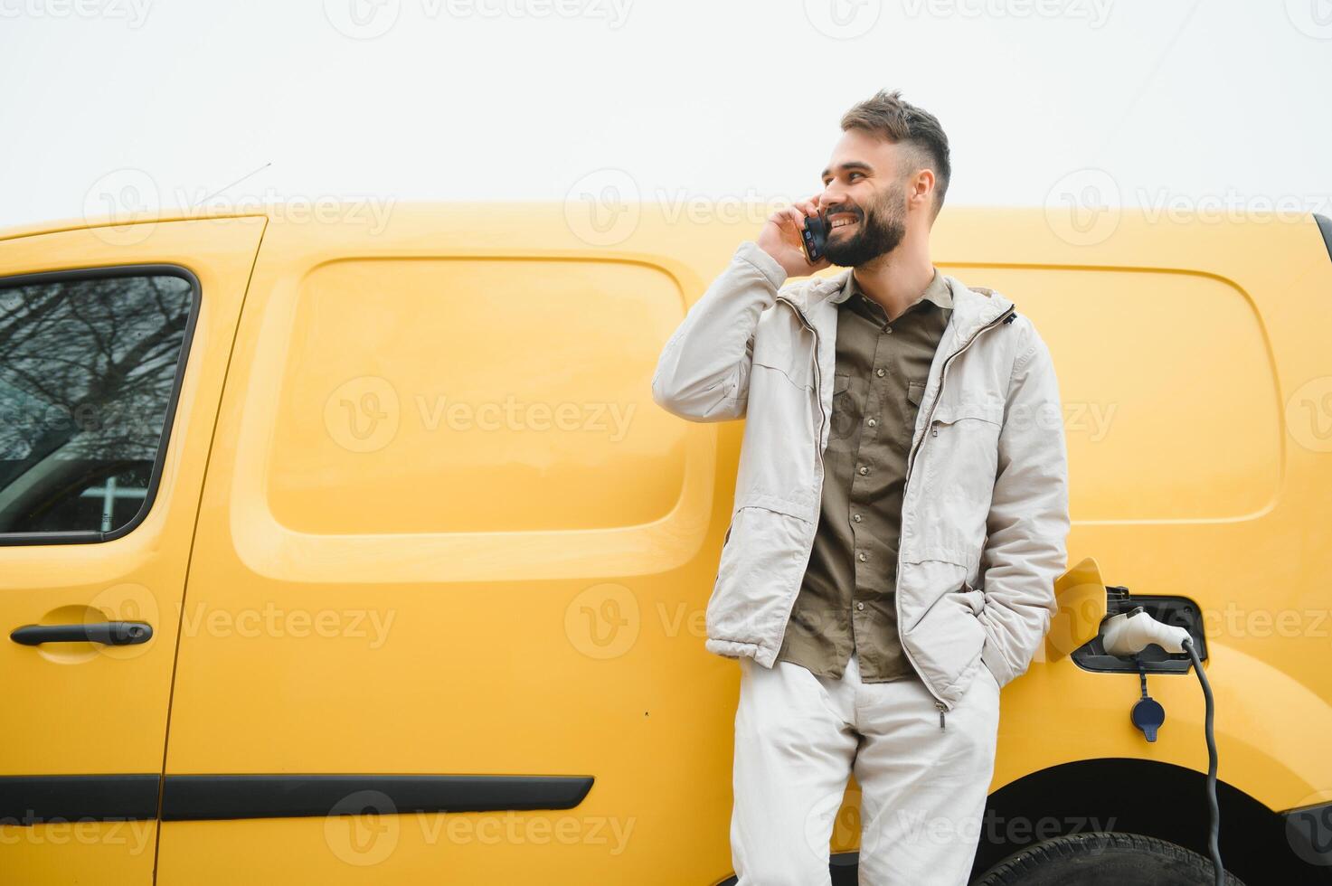 Casual man near electric car waiting for the finish of the battery charging process photo