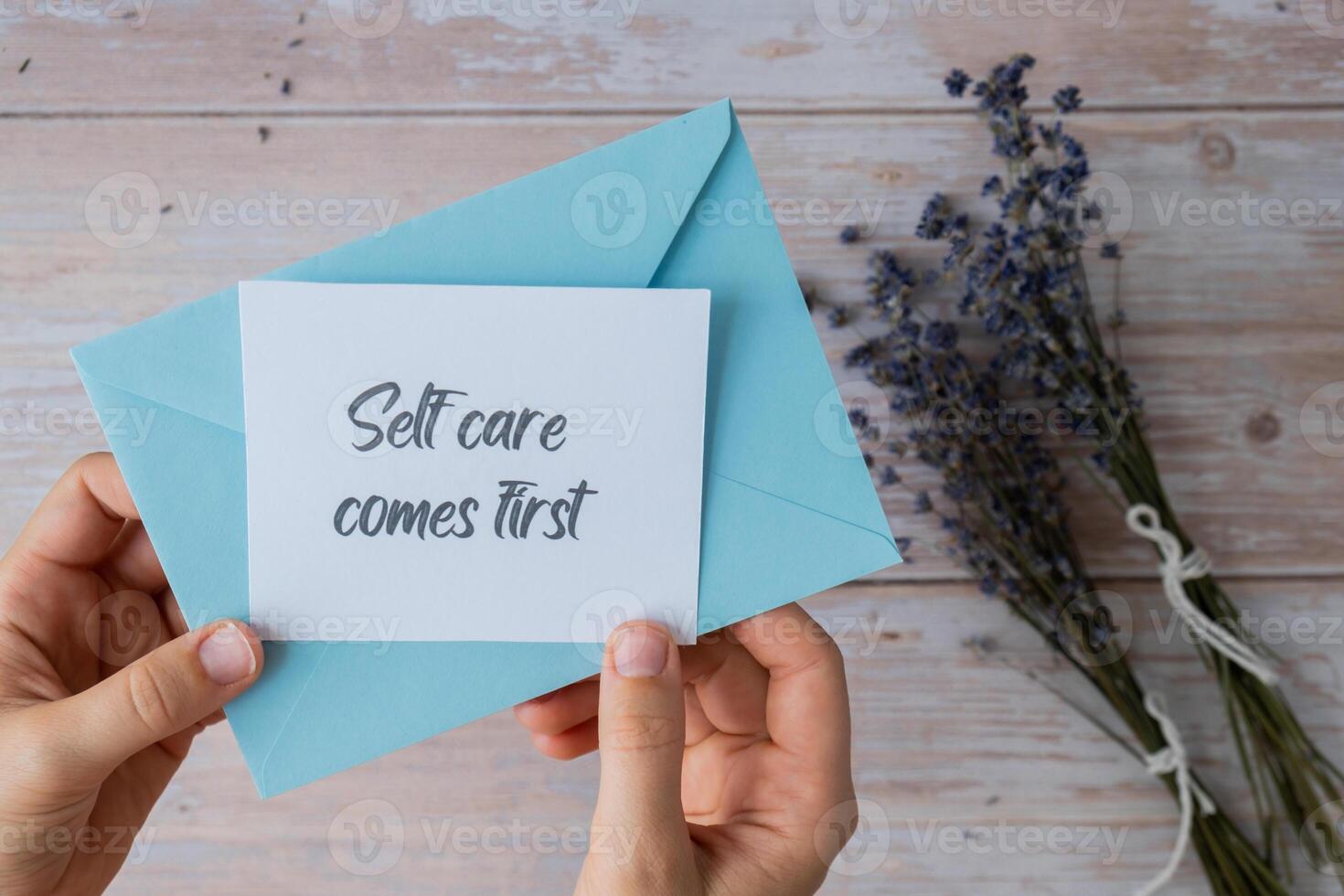 Female hands taking paper card note with text SELF CARE COMES FIRST from blue envelope. Lavender flower. Top view, flat lay. Concept of mental spiritual health self care wellbeing mindfulness photo