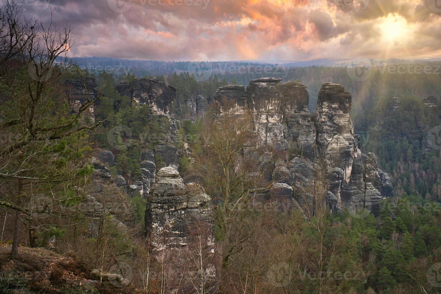 Jagged rocks at the Basteibridge. Wide view over trees and mountains. Dramatic sky photo