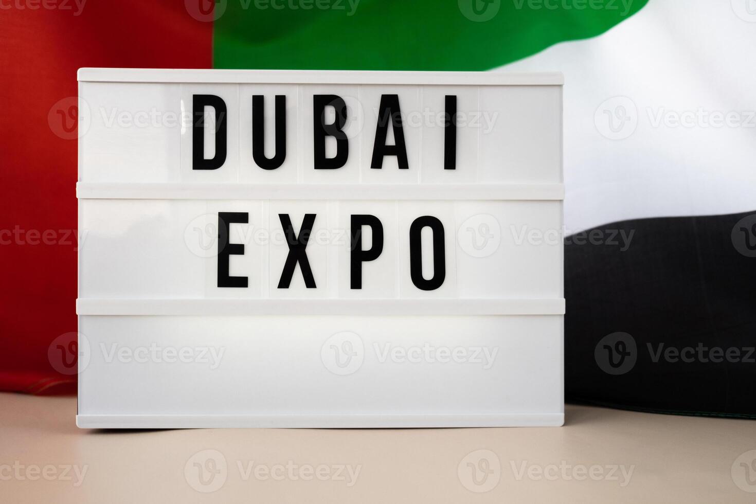 Message text DUBAI EXPO on background of waving UAE flag made from silk. United Arab Emirates flag with concept of tourism and traveling. Inviting greeting card, advertisement. Dubai welcoming card photo