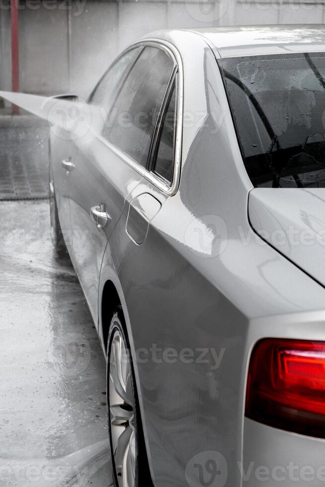 Washing luxury silver car on touchless car wash. Washing sedan car with foam self-service and high pressure water. Cleaning the details of car. Cleanliness and order in urban environment photo