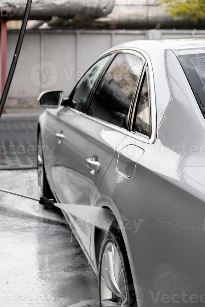 Washing luxury silver car on touchless car wash. Washing sedan car with foam self-service and high pressure water. Cleaning the details of car. Cleanliness and order in urban environment photo