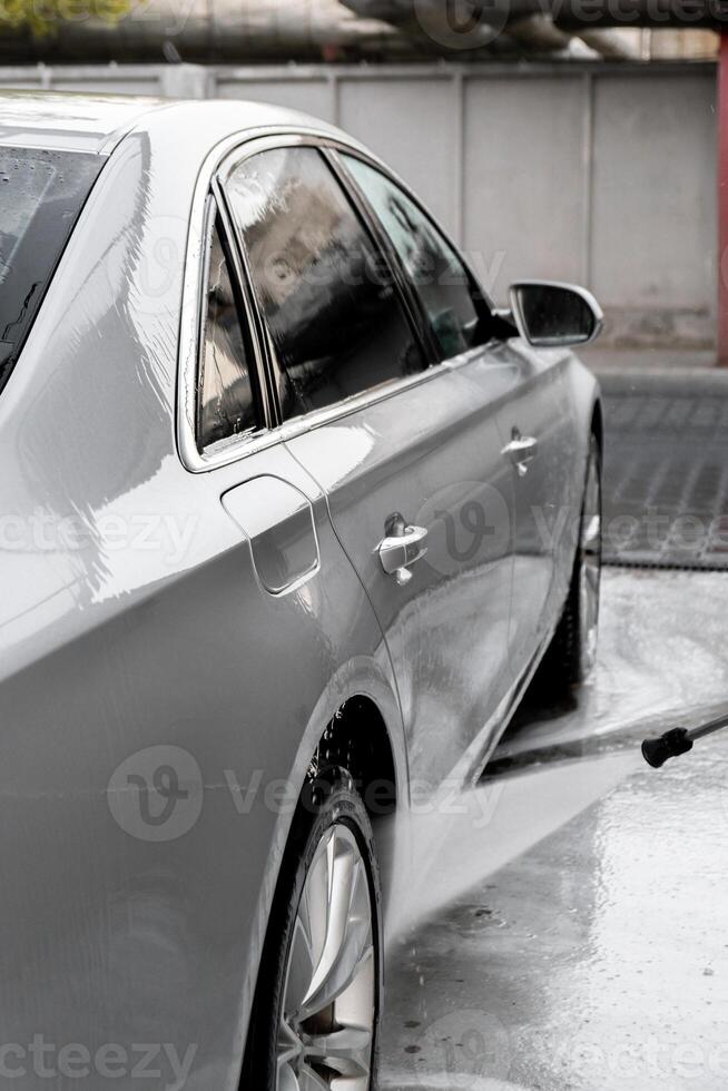 Washing luxury silver car on touchless car wash. Washing sedan car with foam self-service and high pressure water. Cleaning the details of car. Cleanliness and order in urban environment photo