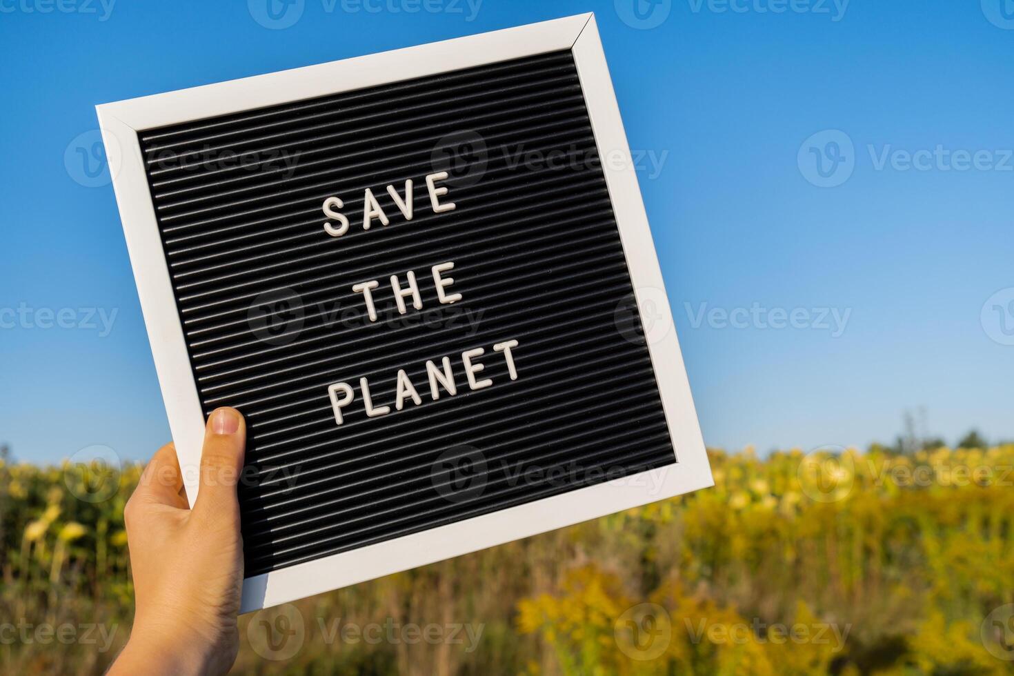 Unrecognizable person with banner message SAVE THE PLANET in sunflower field on sunny day. Sign EARTH day. Concept of ecology and eco activism environmental issues Stop global warming. Go green sustainable photo