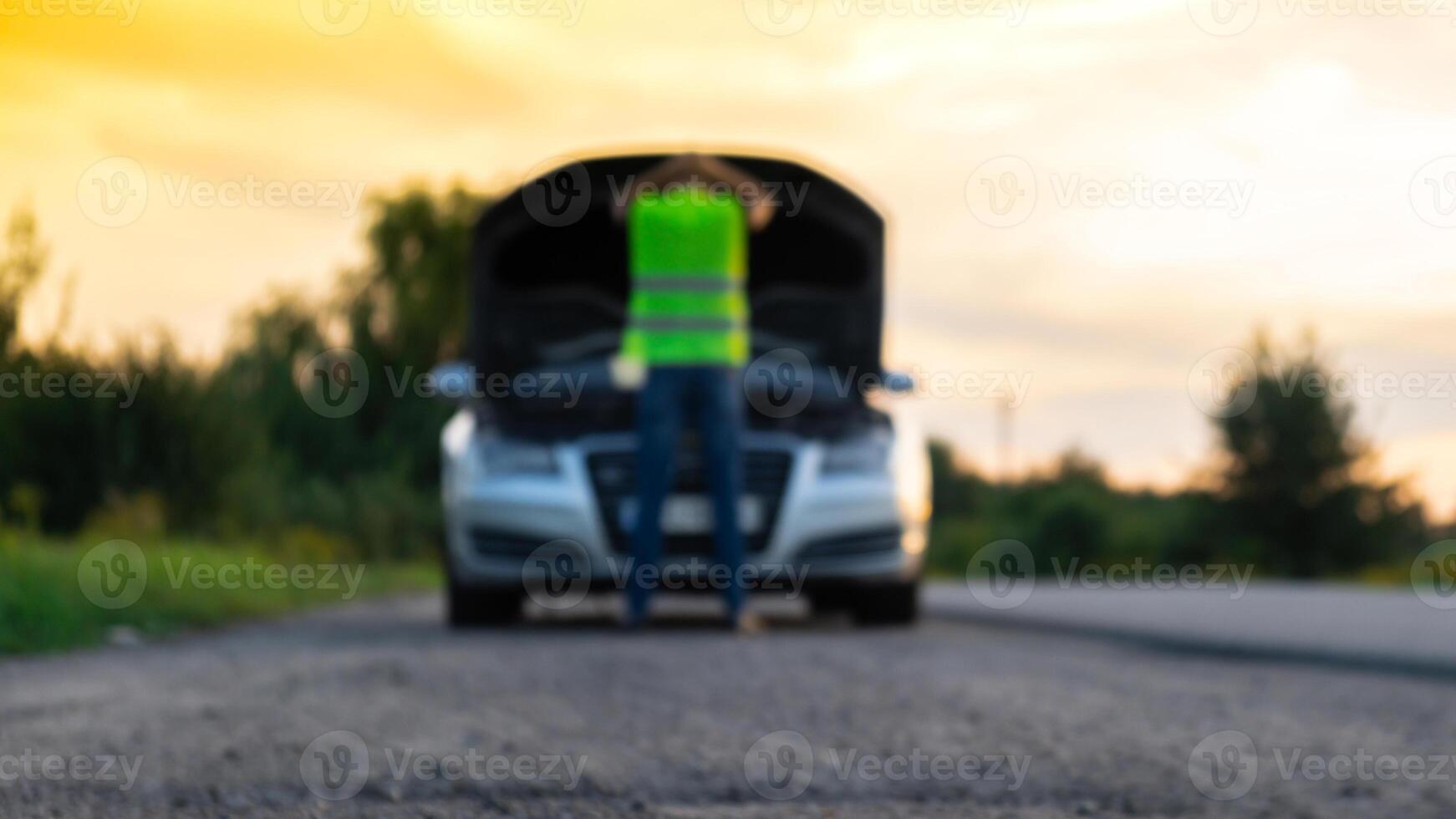 Unrecognizable sad driver in reflective vest. Male driver standing near broken car with open up hood. Red triangle to warn other road users of car breakdown or engine failure stop at countryside highway. Emergency traffic situation photo