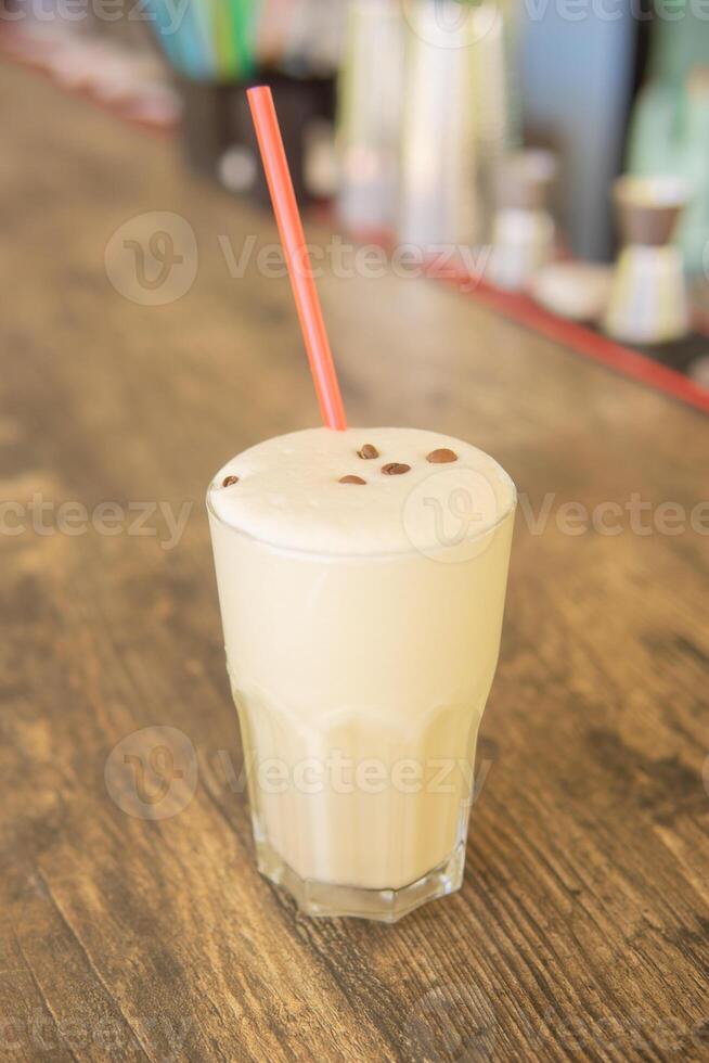 A cold coffee cocktail in a clear glass with a straw on a wooden bar counter photo