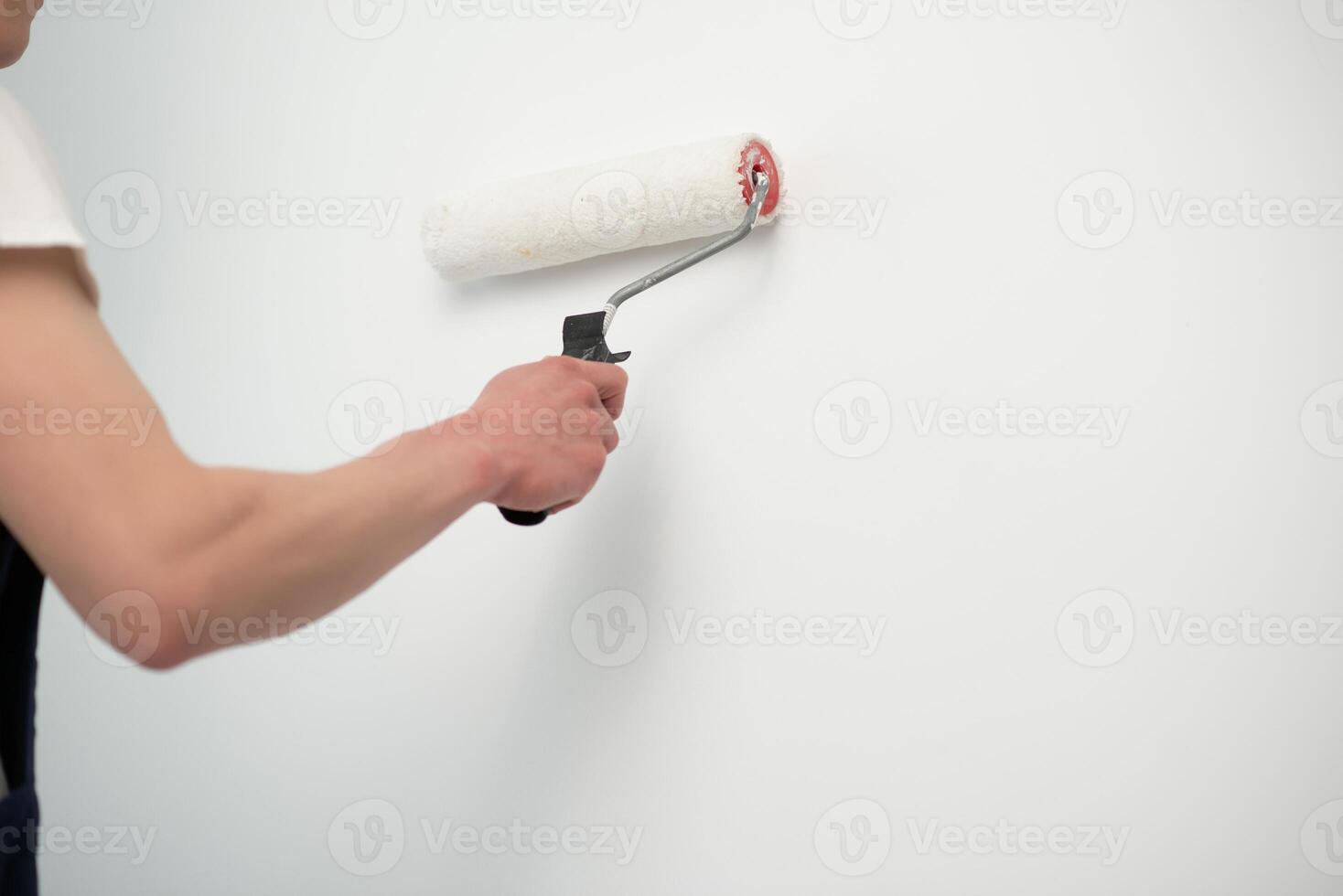 The painter is painting a wall in a room with a roller. photo