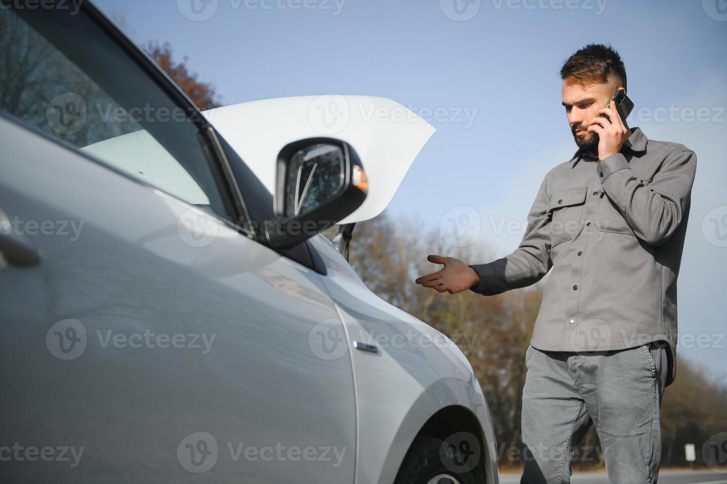 Sad driver calling car service, opening hood, having engine problem standing near broken car on the road. Car breakdown concept photo