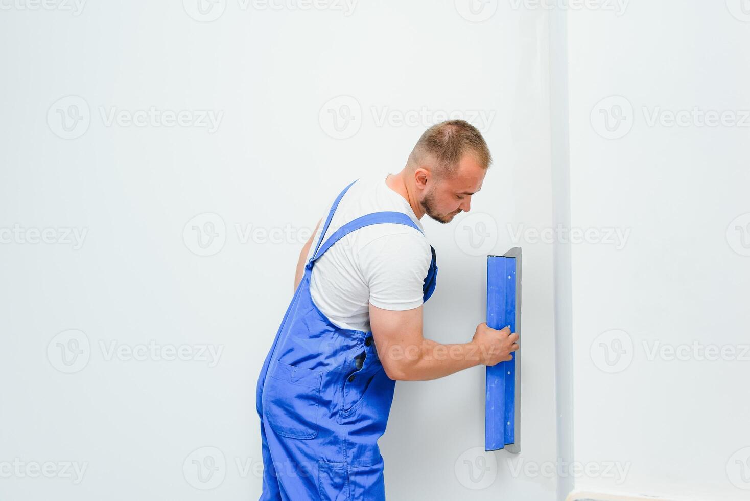 A general laborer in overalls uses a trowel to cover the wall with cement photo